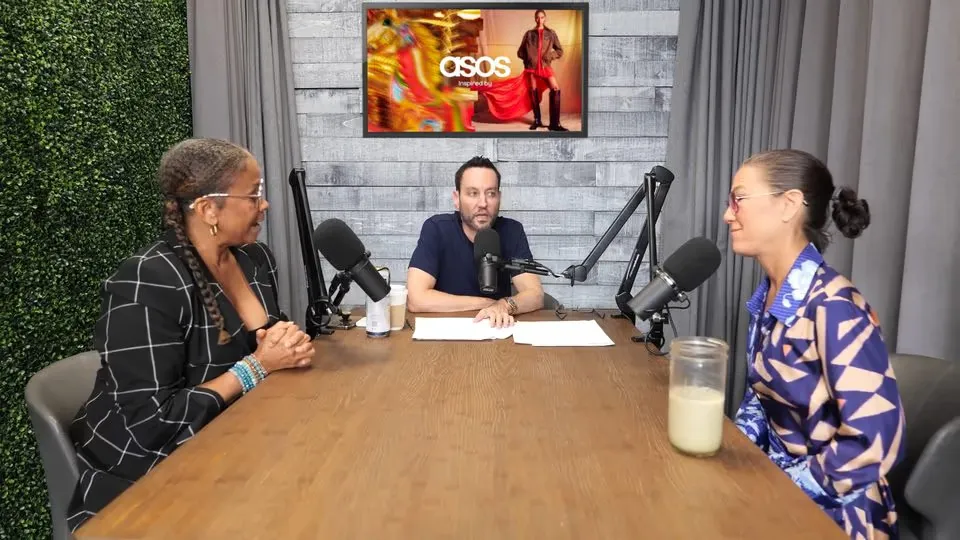 A podcast studio with three people at a table and an ad displayed on the screen behind them