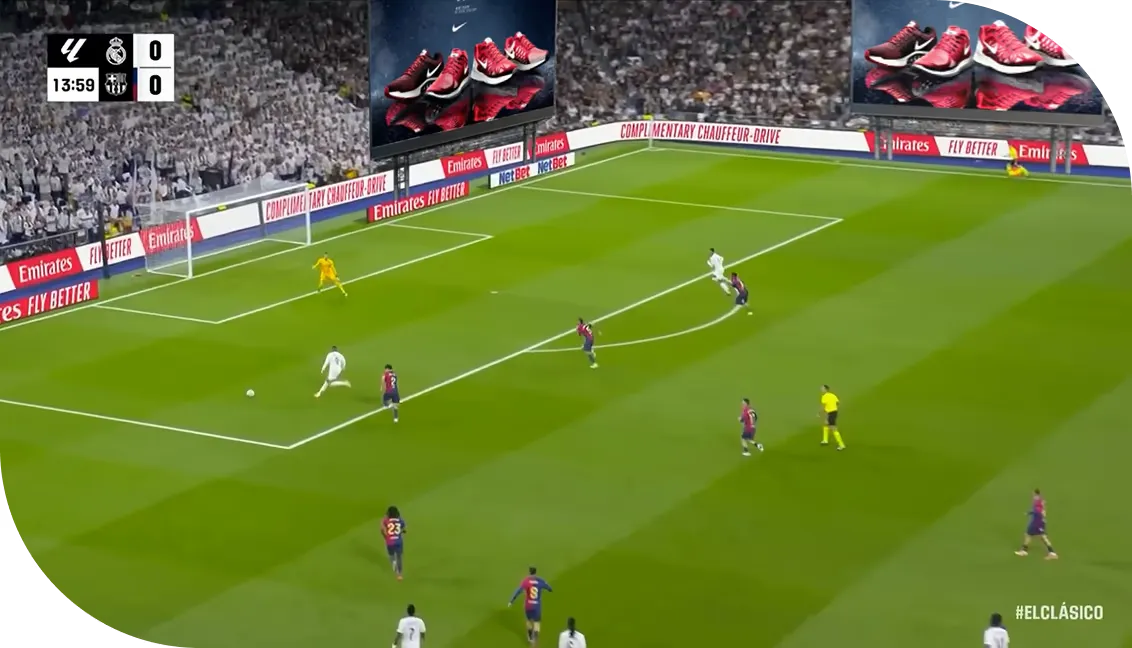Wide shot of a football match in a packed stadium, with ads on the giant screens above the pitch